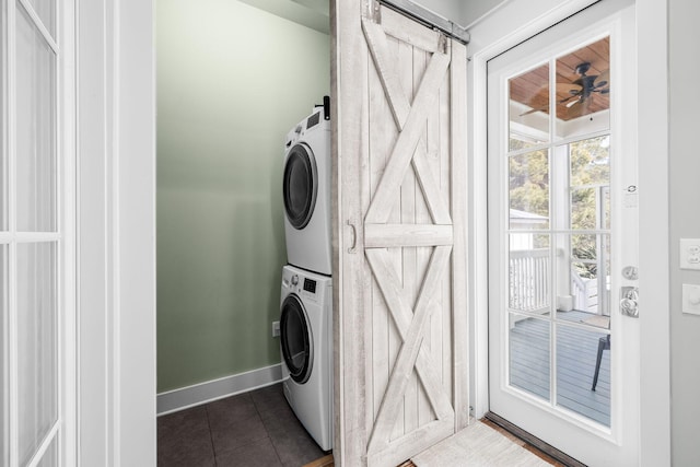 washroom with laundry area, a barn door, baseboards, dark tile patterned flooring, and stacked washer / drying machine