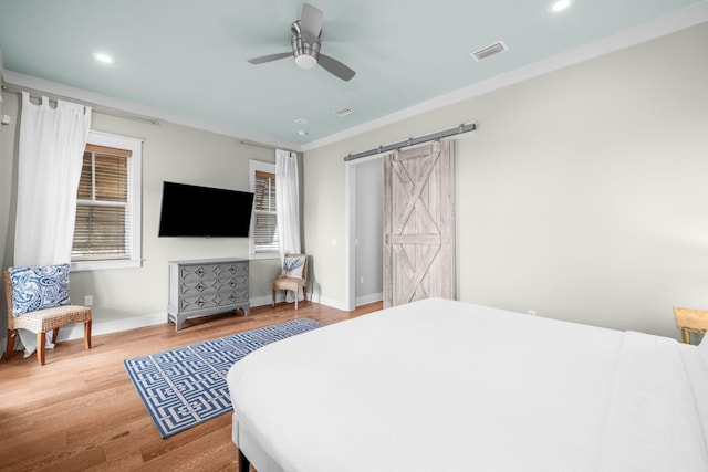 bedroom featuring ceiling fan, a barn door, wood finished floors, visible vents, and baseboards