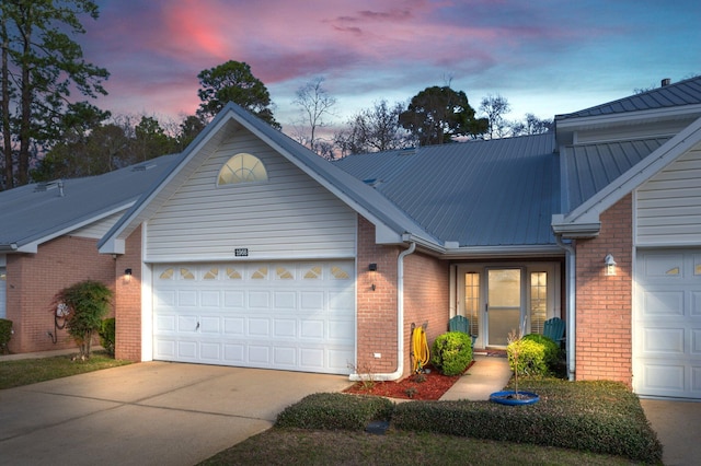 ranch-style house featuring concrete driveway, brick siding, metal roof, and an attached garage