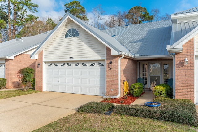 view of front of property featuring a garage, concrete driveway, brick siding, and metal roof