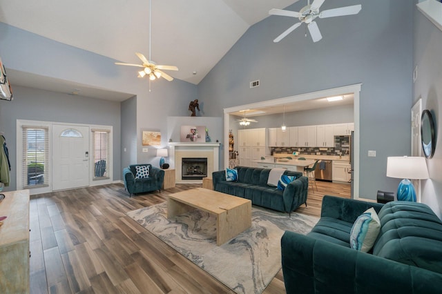 living room with high vaulted ceiling, visible vents, ceiling fan, and wood finished floors