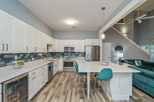 kitchen with wine cooler, stainless steel appliances, white cabinetry, open floor plan, and hanging light fixtures