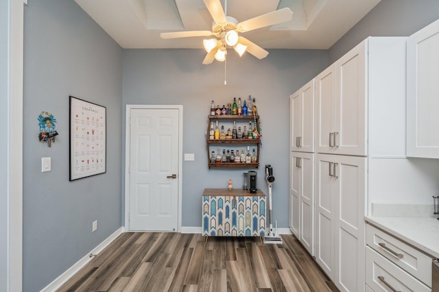 bar with dark wood-type flooring, a ceiling fan, and baseboards