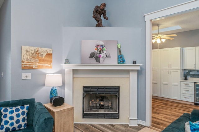 living room featuring beverage cooler, light wood finished floors, a fireplace, and a ceiling fan