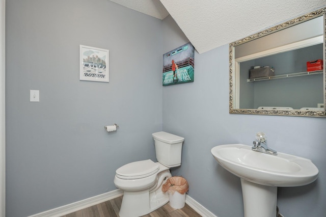 bathroom with a textured ceiling, wood finished floors, toilet, and baseboards