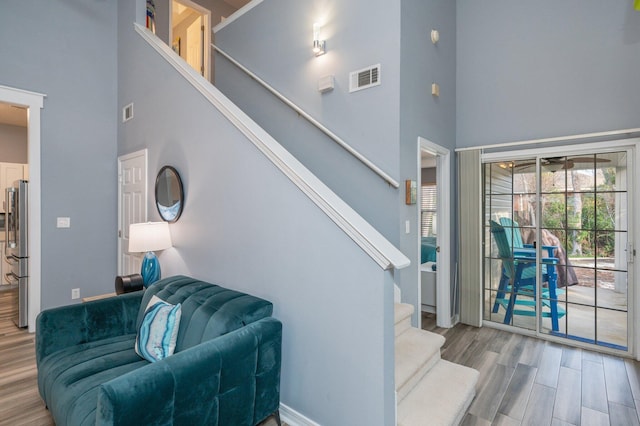 staircase with a towering ceiling, baseboards, visible vents, and wood finished floors