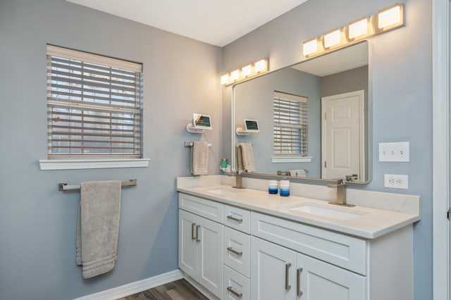 full bath with wood finished floors, a sink, baseboards, and double vanity