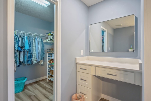 full bath with a spacious closet, a textured ceiling, vanity, wood finished floors, and baseboards