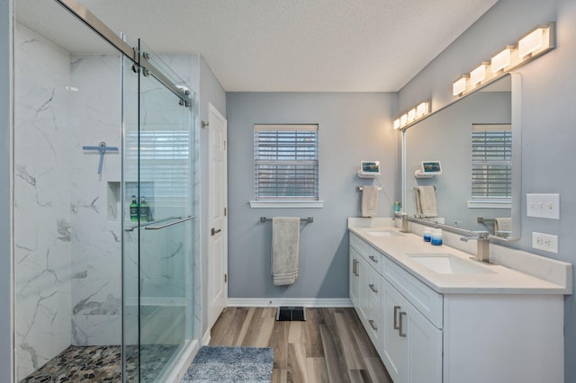 full bathroom featuring double vanity, wood finished floors, a sink, and a marble finish shower