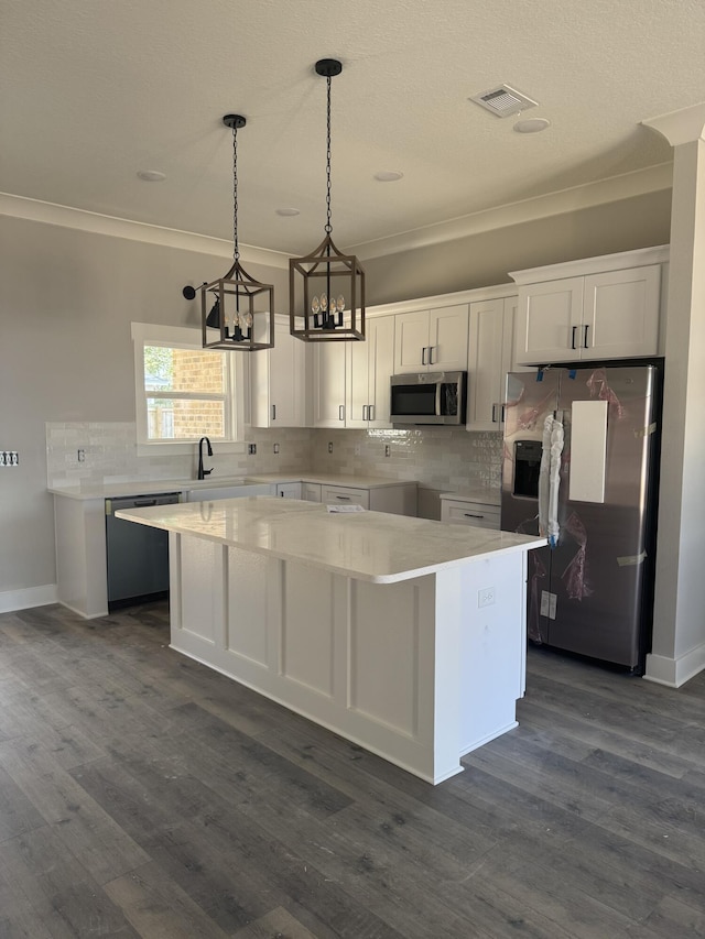 kitchen with stainless steel appliances, white cabinets, a center island, dark wood finished floors, and crown molding