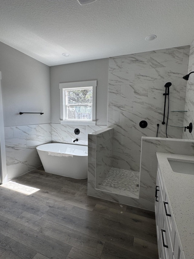 bathroom with a textured ceiling, a freestanding tub, wood finished floors, and a marble finish shower