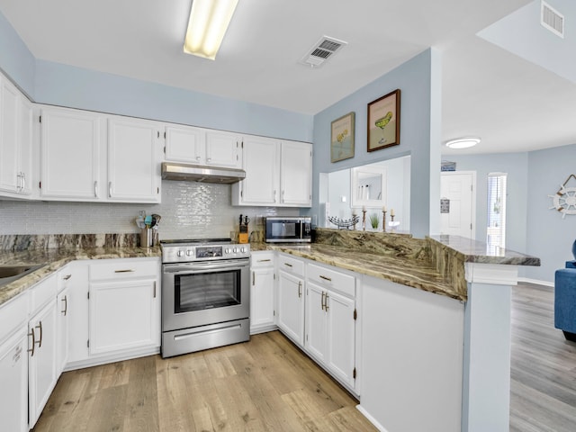 kitchen with stone countertops, under cabinet range hood, a peninsula, visible vents, and appliances with stainless steel finishes