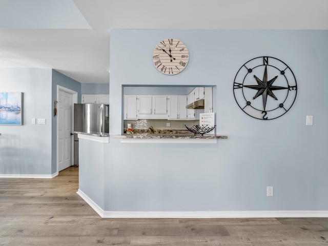 kitchen featuring a peninsula, light wood-style floors, white cabinets, freestanding refrigerator, and tasteful backsplash