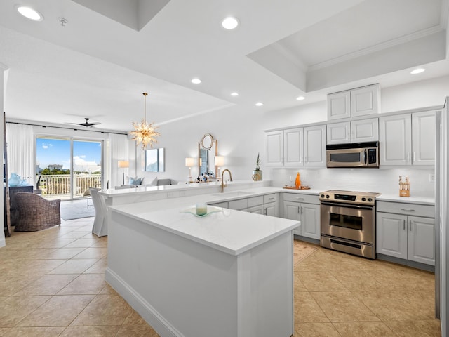 kitchen featuring a raised ceiling, appliances with stainless steel finishes, open floor plan, a sink, and a peninsula