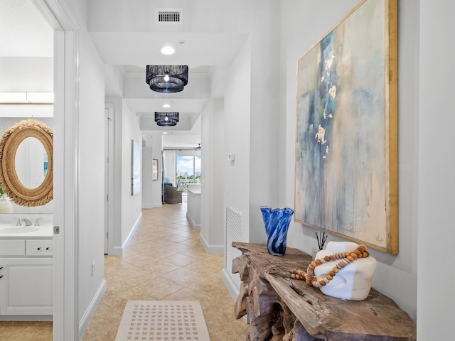 corridor featuring visible vents, a sink, baseboards, and light tile patterned floors