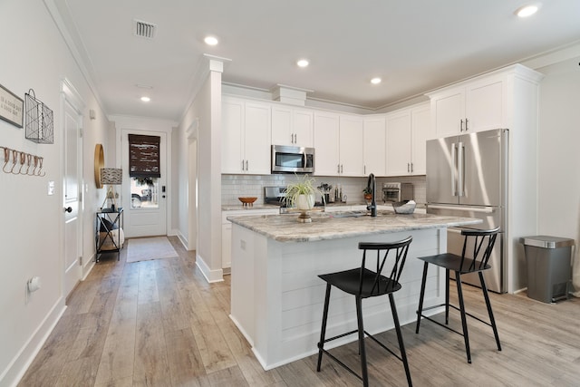 kitchen with stainless steel appliances, light stone counters, a center island with sink, and white cabinets