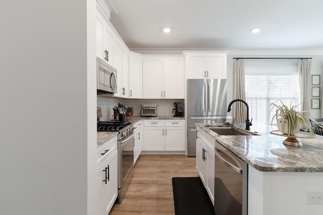 kitchen with appliances with stainless steel finishes, a sink, light stone countertops, white cabinetry, and backsplash