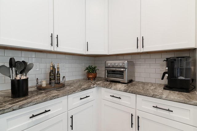 kitchen with a toaster, white cabinetry, decorative backsplash, and dark stone countertops