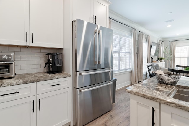 kitchen featuring light stone counters, white cabinets, backsplash, a wealth of natural light, and freestanding refrigerator