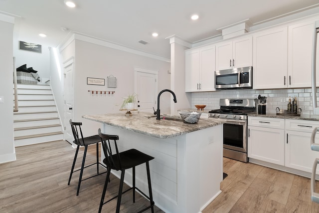 kitchen with appliances with stainless steel finishes, an island with sink, light stone counters, and white cabinets