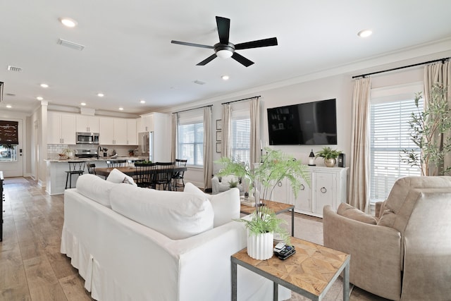 living room with light wood-type flooring, visible vents, crown molding, and recessed lighting