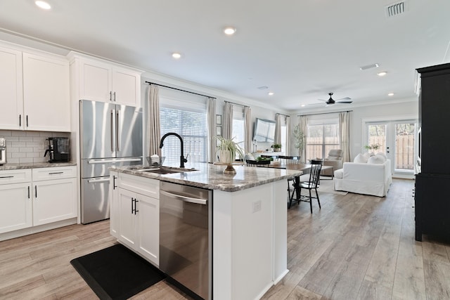 kitchen with a center island with sink, stainless steel appliances, visible vents, open floor plan, and white cabinetry