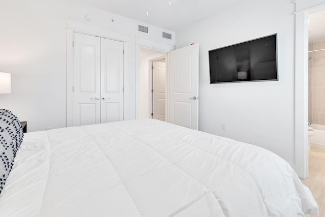 bedroom featuring light wood-type flooring, a closet, visible vents, and ensuite bathroom