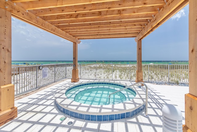 view of pool with a patio, a water view, a view of the beach, and a hot tub