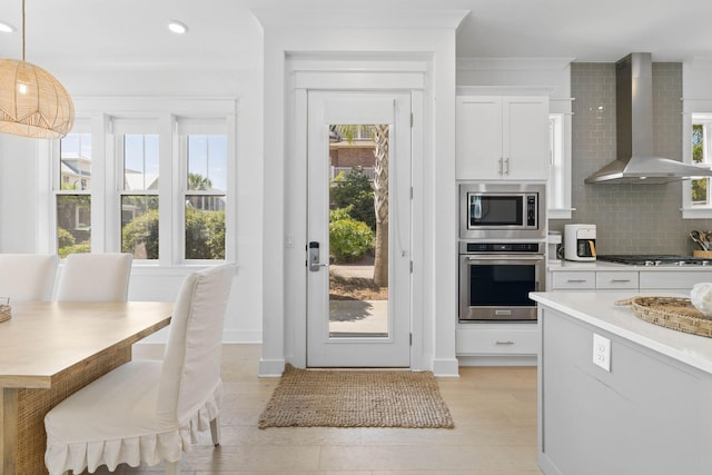 kitchen featuring tasteful backsplash, white cabinets, appliances with stainless steel finishes, wall chimney range hood, and a wealth of natural light