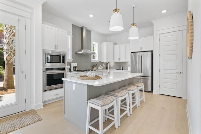 kitchen featuring white cabinets, light countertops, appliances with stainless steel finishes, wall chimney range hood, and decorative backsplash