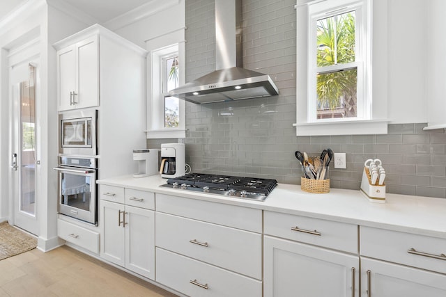 kitchen with a healthy amount of sunlight, wall chimney range hood, white cabinets, and stainless steel appliances