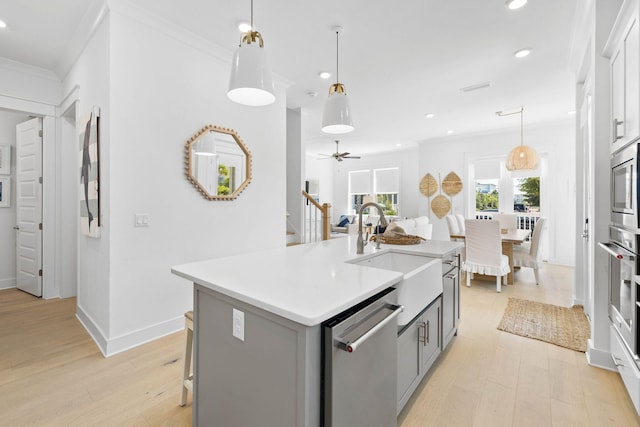 kitchen featuring stainless steel appliances, light countertops, light wood-style flooring, ornamental molding, and a sink