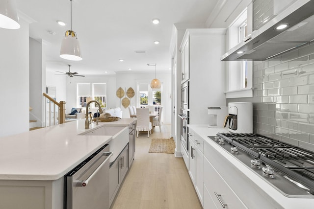 kitchen with stainless steel appliances, a sink, exhaust hood, open floor plan, and hanging light fixtures