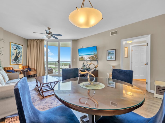 dining space featuring visible vents, ceiling fan, baseboards, light wood-type flooring, and a wall of windows