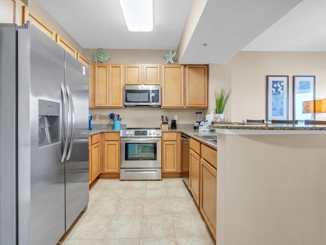 kitchen featuring light stone counters, appliances with stainless steel finishes, a peninsula, and light brown cabinetry