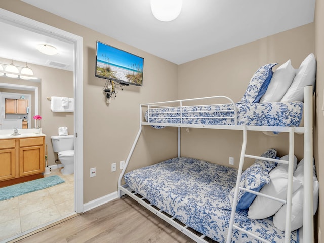 bedroom with visible vents, light wood-style flooring, a sink, connected bathroom, and baseboards