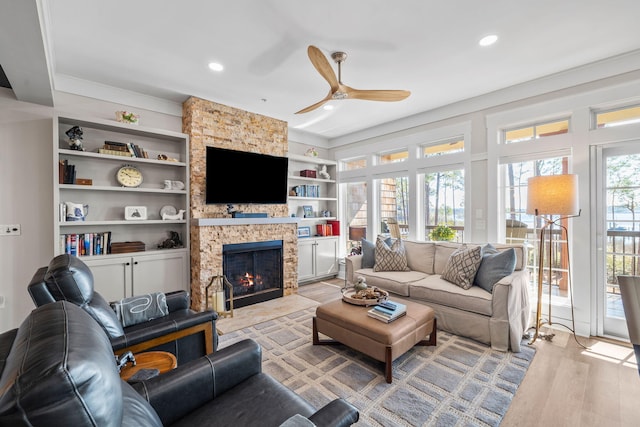 living room with built in shelves, recessed lighting, a fireplace, a ceiling fan, and light wood-type flooring