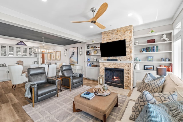 living area featuring built in shelves, light wood finished floors, recessed lighting, a ceiling fan, and a stone fireplace