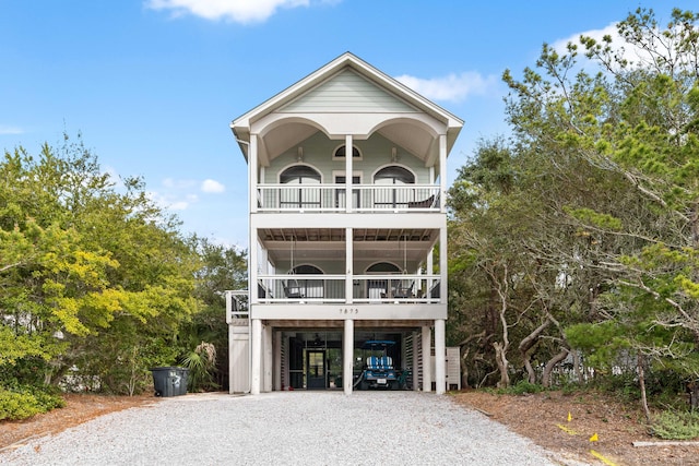 coastal inspired home with gravel driveway, a balcony, and a carport