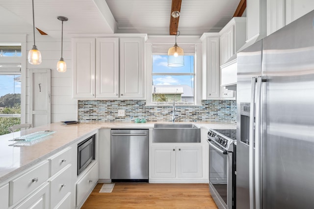 kitchen featuring decorative light fixtures, stainless steel appliances, white cabinetry, a sink, and light stone countertops