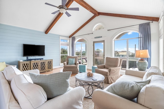 living room with high vaulted ceiling, wood walls, a ceiling fan, beam ceiling, and light wood finished floors