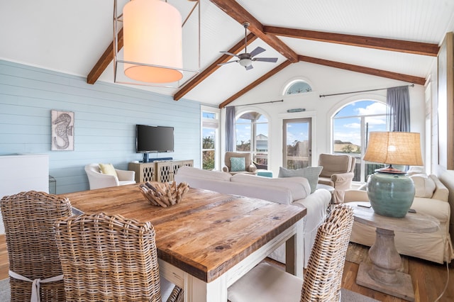 dining space featuring vaulted ceiling with beams, wood walls, a ceiling fan, and wood finished floors