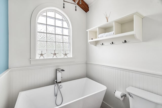 full bathroom with a freestanding bath, a wainscoted wall, and toilet