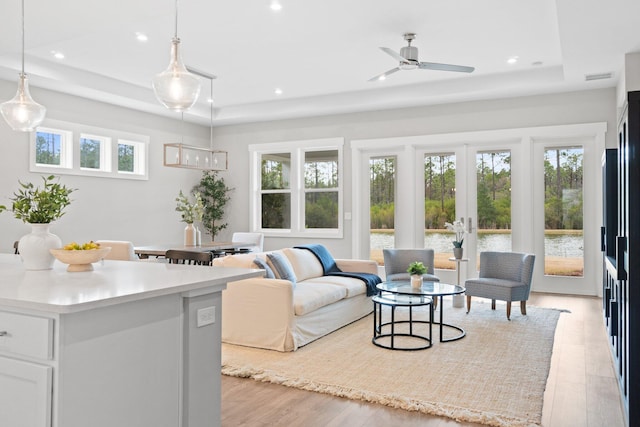 living room featuring a healthy amount of sunlight, light wood finished floors, visible vents, and a tray ceiling