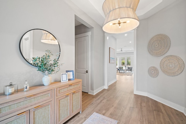 corridor featuring a chandelier, light wood-style flooring, and baseboards