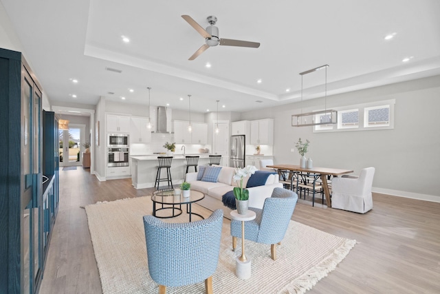 living room with light wood finished floors, baseboards, a raised ceiling, and recessed lighting