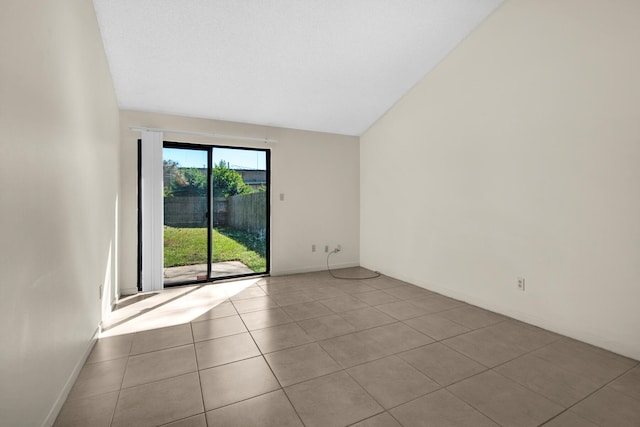 unfurnished room featuring light tile patterned flooring, vaulted ceiling, and baseboards