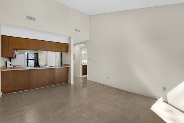 interior space featuring tile patterned flooring, a peninsula, visible vents, light countertops, and brown cabinetry