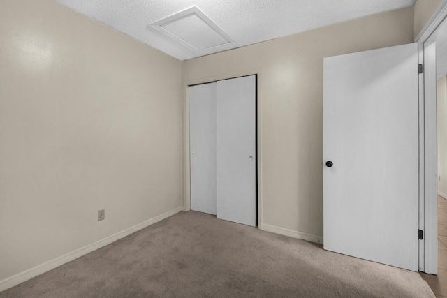 unfurnished bedroom with baseboards, a closet, attic access, and light colored carpet