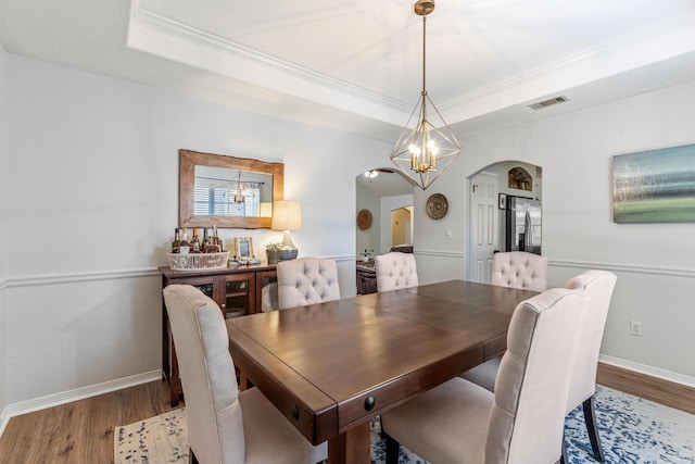 dining room with visible vents, arched walkways, a raised ceiling, and wood finished floors